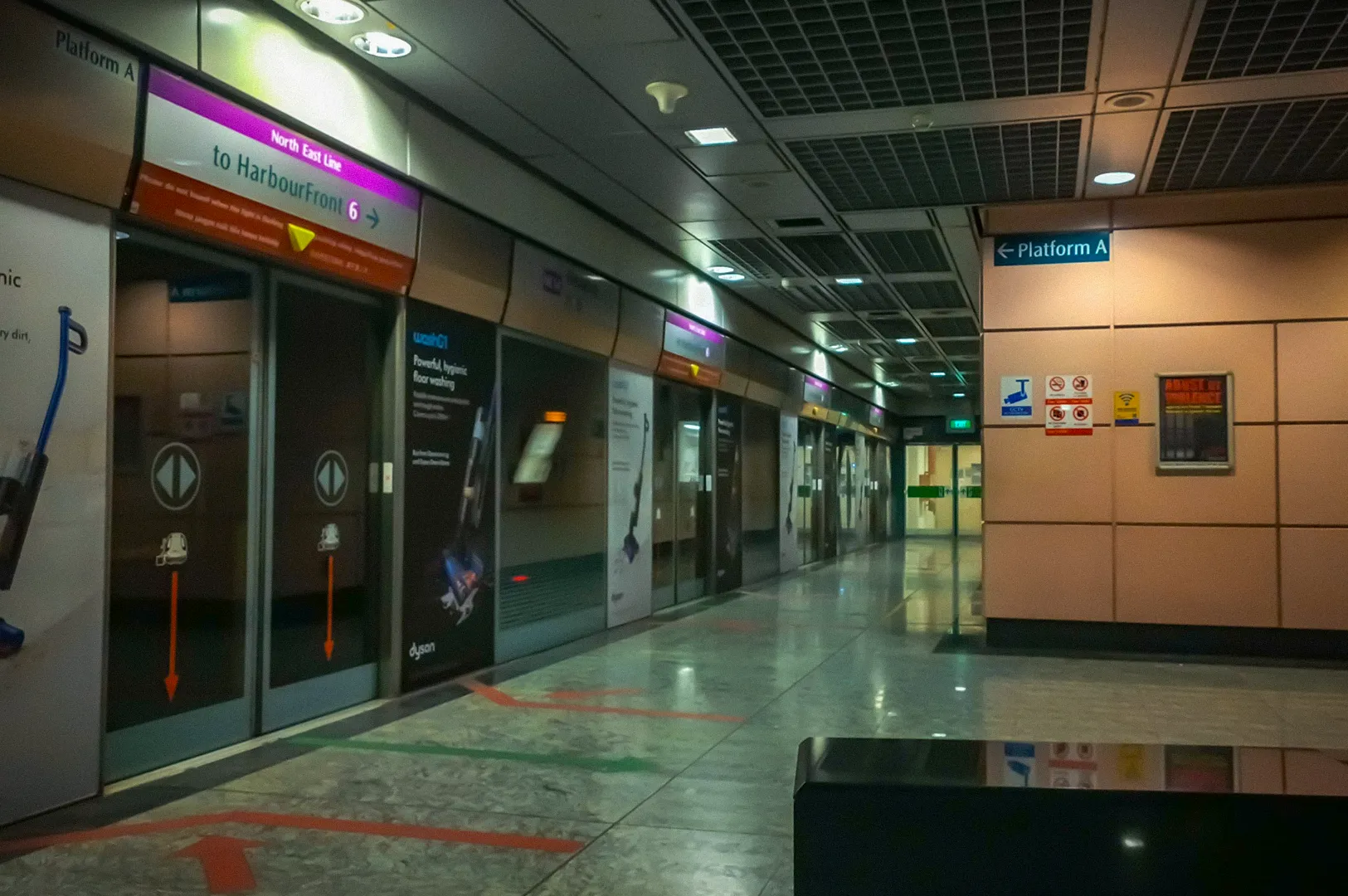 North East Line MRT platform with screen doors, directional signage, and waiting area inside a modern underground train station.