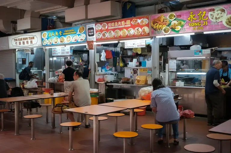 Traditional Singapore hawker centre with local food stalls, communal seating, and diners enjoying affordable meals in a neighborhood food court.