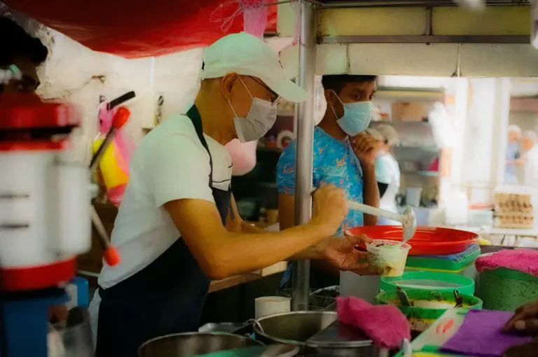 Singapore hawker food vendor preparing a local dish at a busy street food stall with customers and cooking equipment in view.