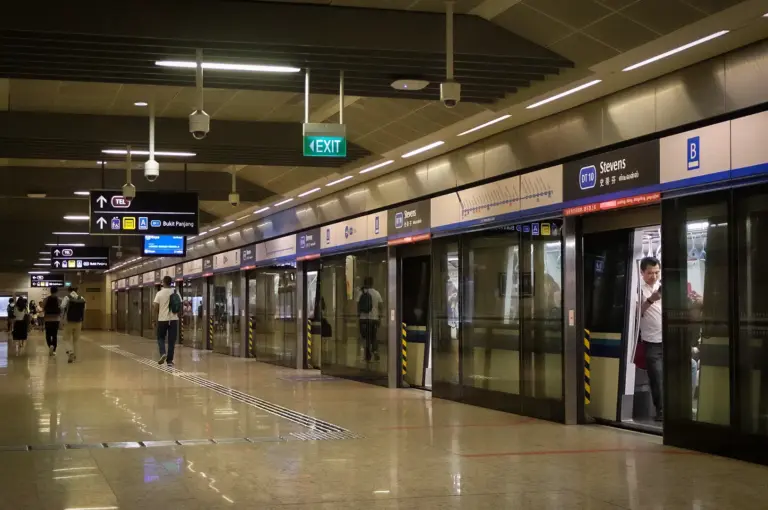 Stevens MRT Station platform in Singapore featuring modern platform screen doors, clear wayfinding signs, and commuters boarding a Downtown Line train.
