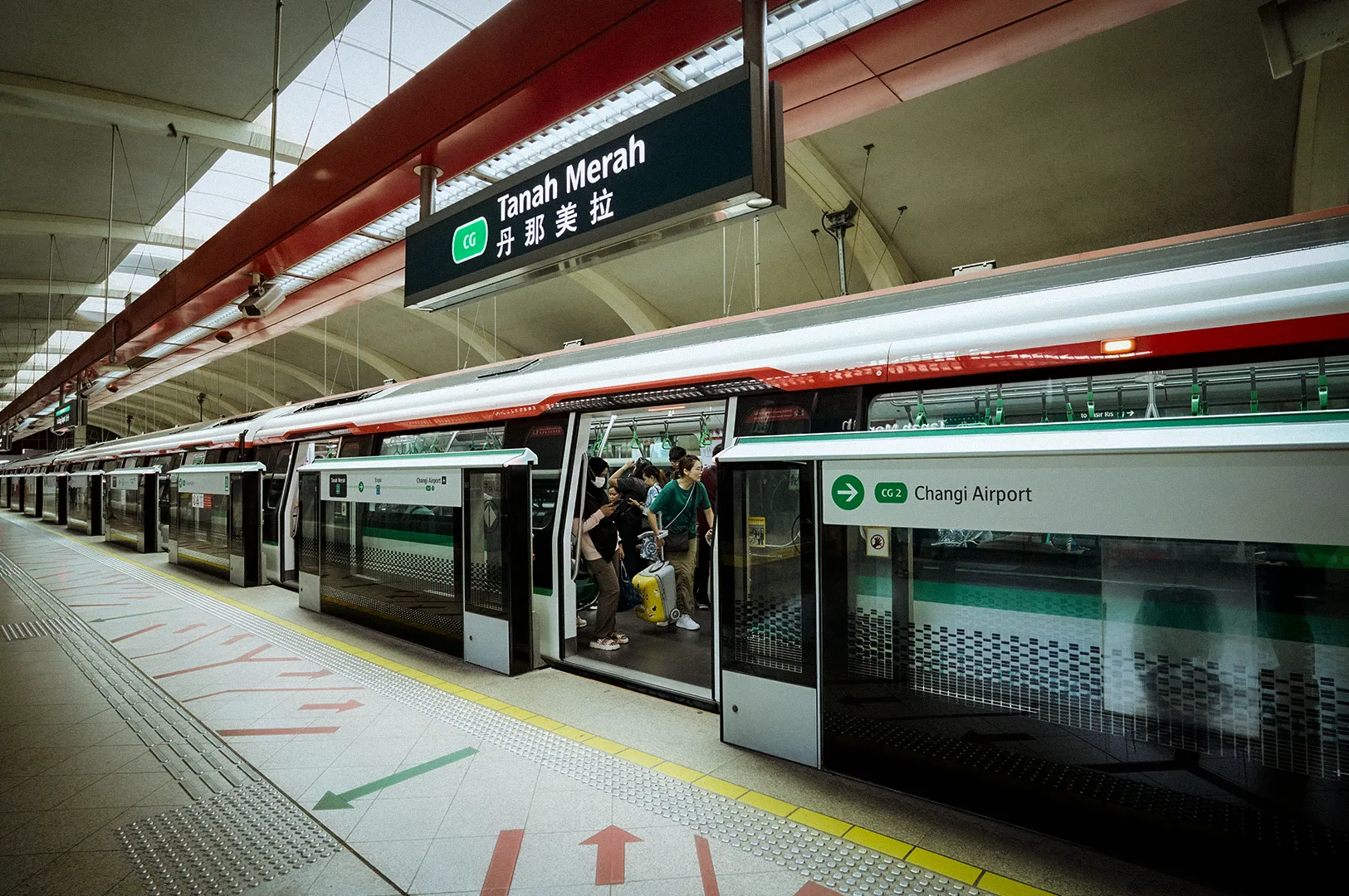 Tanah Merah MRT Station platform in Singapore with passengers boarding a train and directional signage toward Changi Airport.