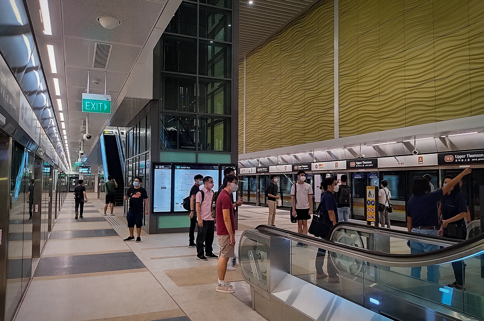 Passengers waiting on the platform at Upper Thomson MRT Station in Singapore, featuring the Thomson-East Coast Line’s modern underground design, platform screen doors, escalators, and directional signage.