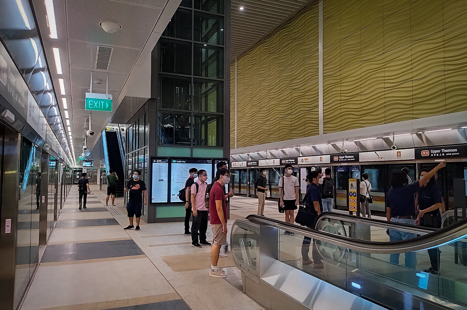 Upper Thomson MRT Station platform in Singapore featuring modern underground transit architecture, platform screen doors, escalators, and commuters waiting for the train.