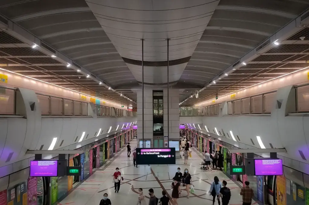 Elevated view of Kovan MRT Station in Singapore, showing modern train platforms, passenger walkways, digital signage, and commuters using the North East Line.