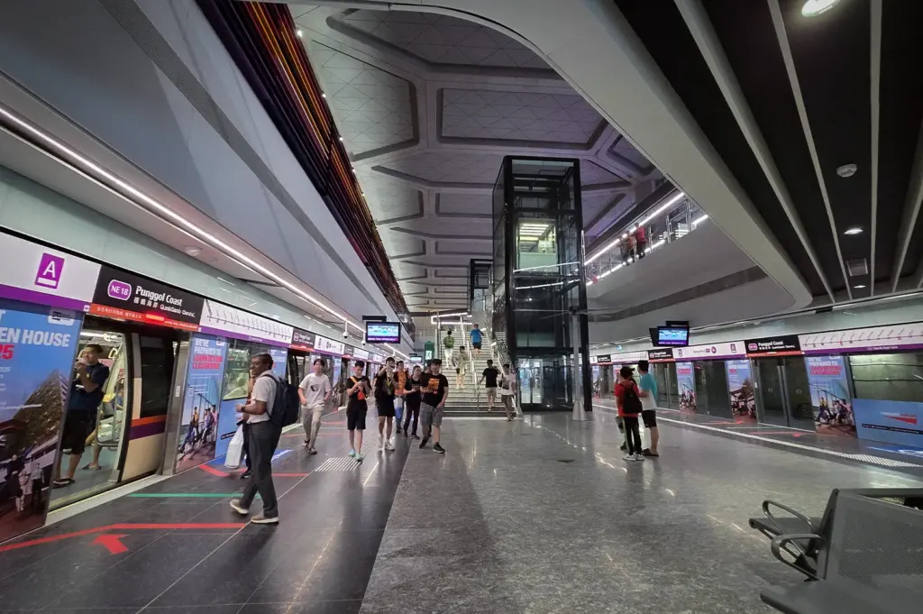 Punggol Coast MRT Station platform in Singapore featuring modern architecture, platform screen doors, escalators, and waiting passengers.