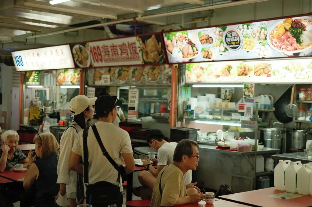 Customers dining and queuing at a Hainanese chicken rice stall in a Singapore hawker centre, showcasing local food culture and traditional food court dining.