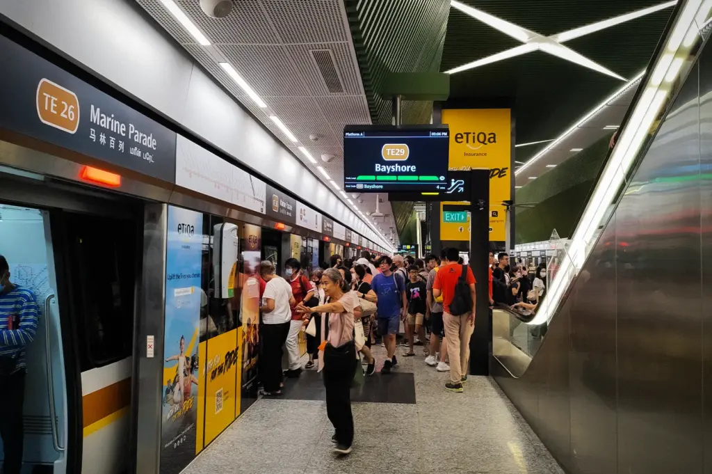 Commuters waiting on the platform at Marine Parade MRT Station in Singapore, featuring Thomson-East Coast Line signage, platform screen doors, modern station architecture, and passengers boarding the train.
