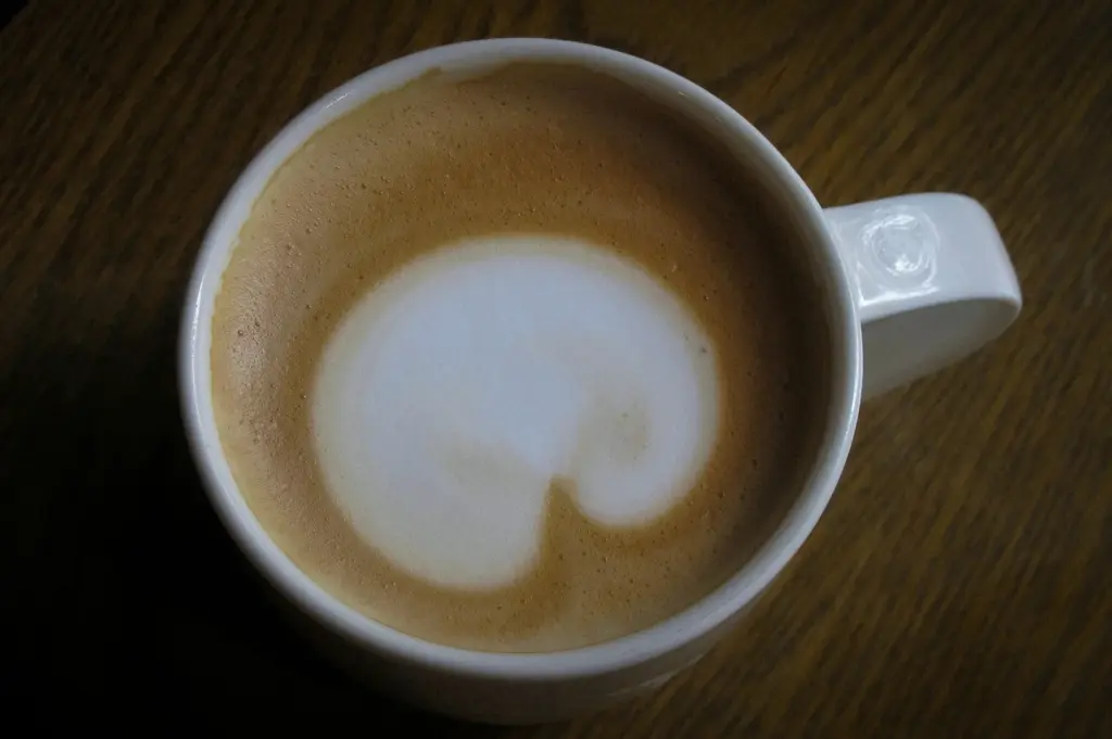 Close-up top view of a creamy latte with heart-shaped latte art in a white coffee cup on a dark wooden table in a cozy cafe setting