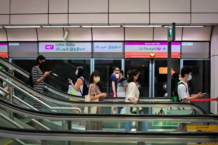 Commuters riding escalators inside Little India MRT Station in Singapore with platform screen doors, station signage, and modern public transport infrastructure.