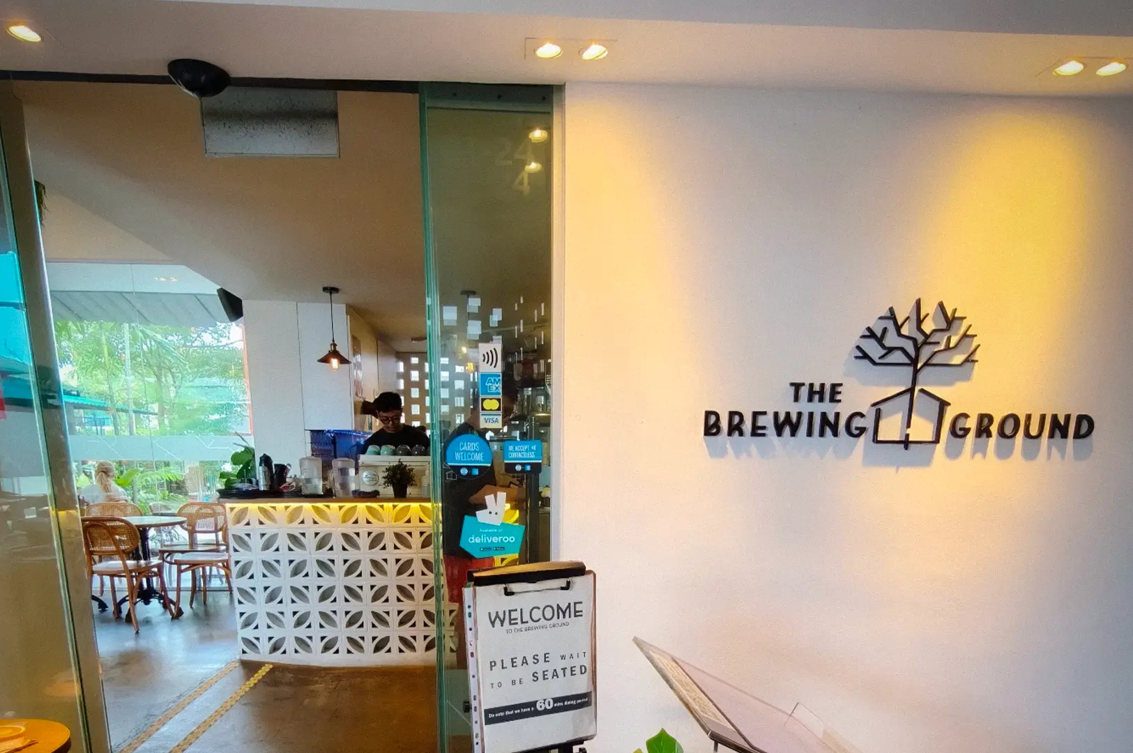Entrance of The Brewing Ground in Joo Chiat, Singapore, featuring its modern café facade, welcoming signage, and cozy interior visible through glass doors.