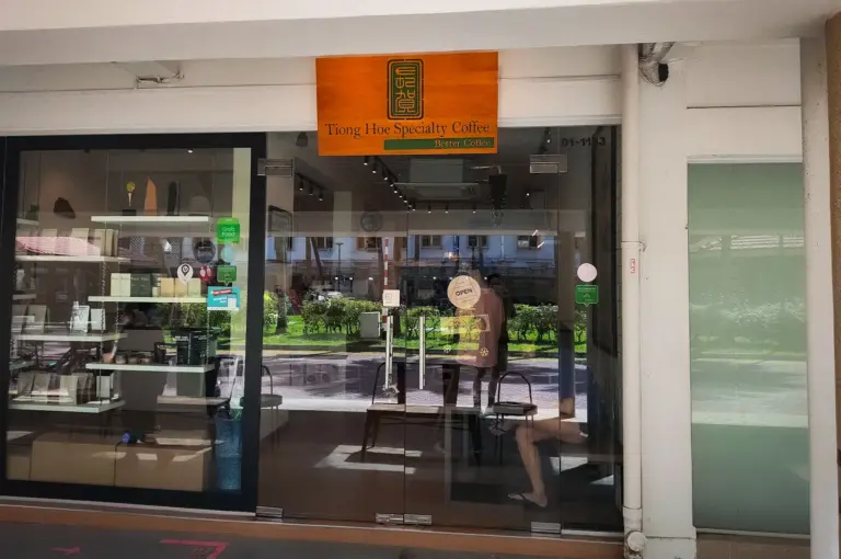 Entrance of Tiong Hoe Specialty Coffee in Singapore featuring a modern glass storefront, coffee retail display, and welcoming café entrance beneath its signature wooden sign.