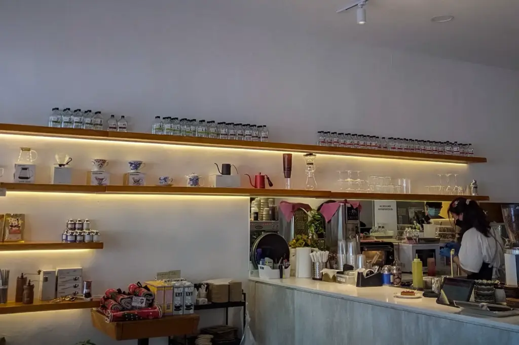 Coffee bar at Kings Cart Coffee Factory in Singapore showcasing minimalist shelving, specialty brewing equipment, artisan coffee products, and baristas preparing fresh coffee.