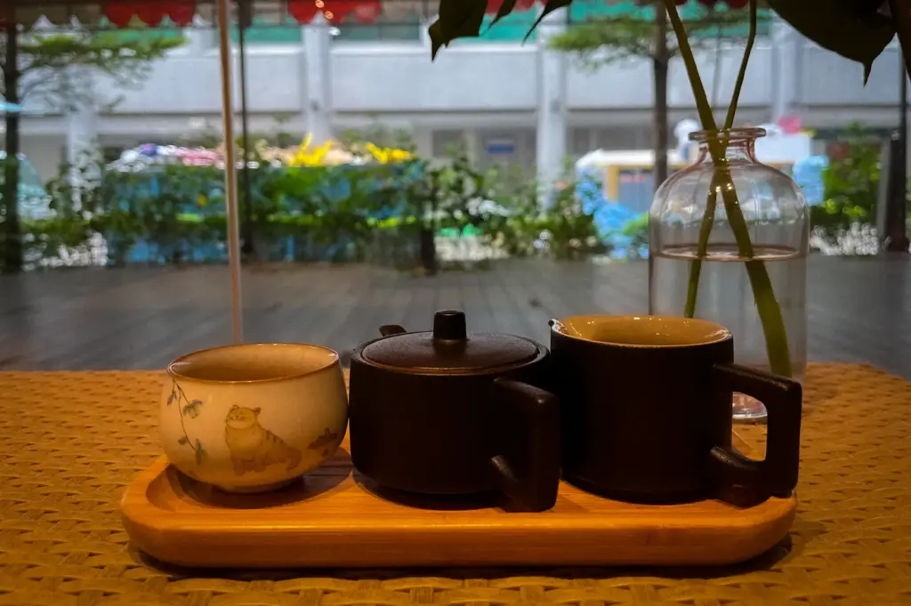 Traditional tea set served at PACTO by Parchmen Singapore, featuring a teapot and ceramic cups on a wooden tray beside a minimalist table setting with greenery.