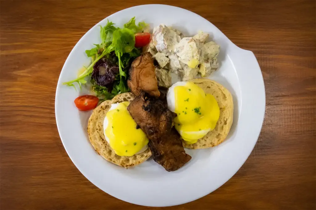 Classic eggs Benedict with poached eggs, hollandaise sauce, sautéed mushrooms, fresh salad, and creamy potato salad served on toasted English muffins at The Basement Cafe.