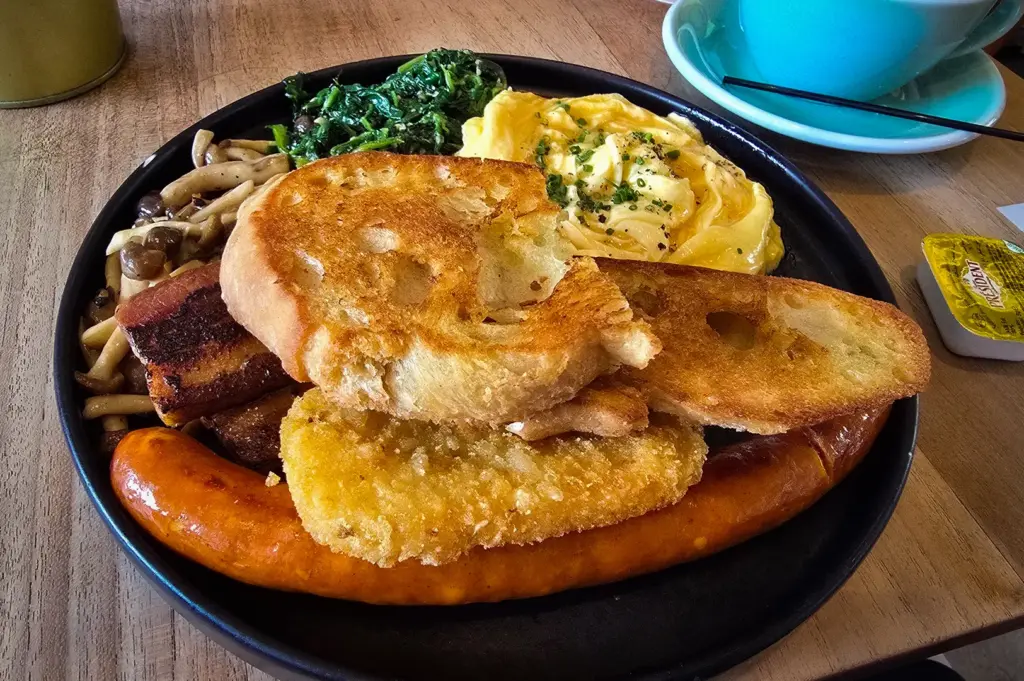 Hearty big breakfast at The Brewing Ground Singapore with sausage, bacon, scrambled eggs, mushrooms, spinach, hash brown, toasted sourdough, and black coffee.