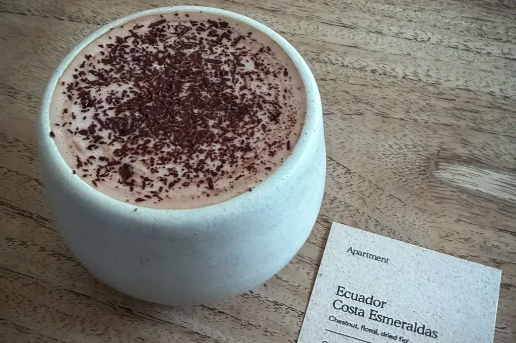 Signature chocolate drink served in a handcrafted ceramic cup at Apartment Coffee Singapore with an Ecuador Costa Esmeraldas chocolate tasting card on a wooden table.