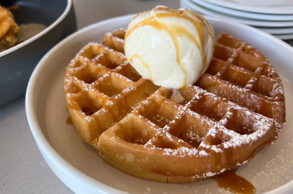 Golden waffle topped with vanilla ice cream, caramel sauce, and powdered sugar served as a dessert at Atlas Coffeehouse in Bukit Timah, Singapore.