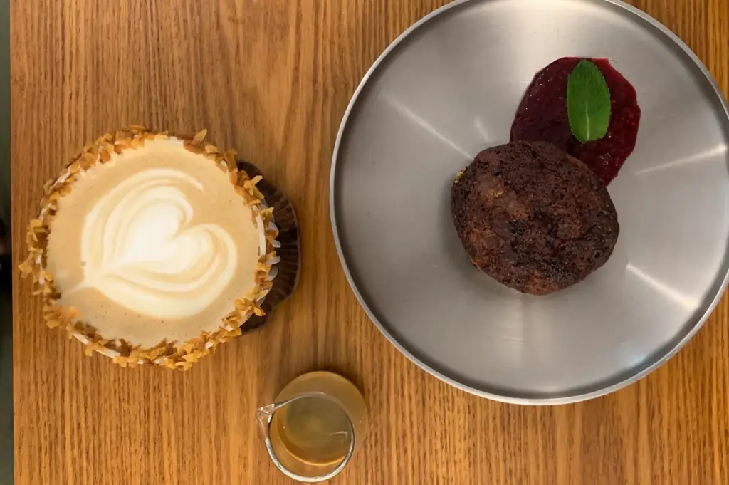 Overhead view of a specialty latte with latte art, espresso shot, and chocolate dessert served at Kings Cart Coffee Factory in Singapore on a wooden table.