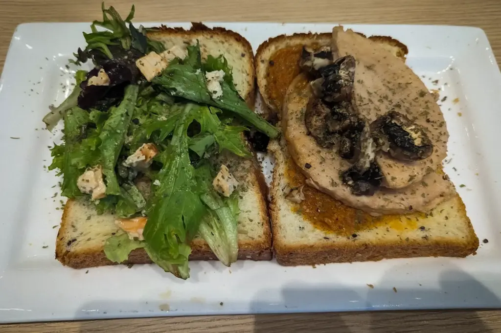 Open-faced sandwich served at PACTO by Parchmen Singapore with sliced roasted meat, sautéed mushrooms, mixed greens, artisan bread, and fresh salad on a white plate.