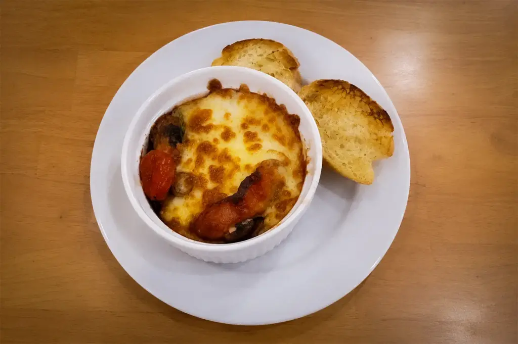 Baked cheese breakfast casserole with roasted tomatoes, mushrooms, melted cheese, and toasted artisan bread served fresh at The Basement Cafe.