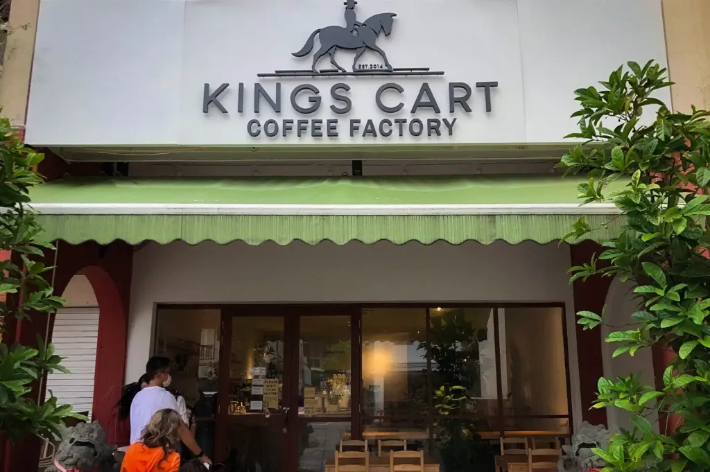 Front entrance of Kings Cart Coffee Factory in Singapore featuring the café's signage, outdoor seating, lush greenery, and welcoming storefront along a neighborhood street.