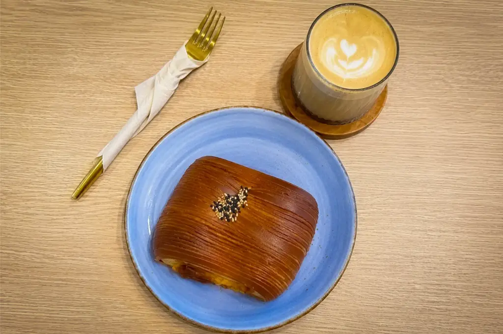 Luncheon meat puff pastry served at PACTO by Parchmen Singapore with a latte featuring heart latte art, presented on a blue plate in a modern café setting.