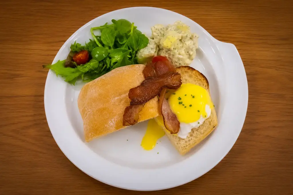 Poached eggs Benedict with crispy bacon, hollandaise sauce, fresh garden salad, creamy potato salad, and toasted bread served at The Basement Cafe.