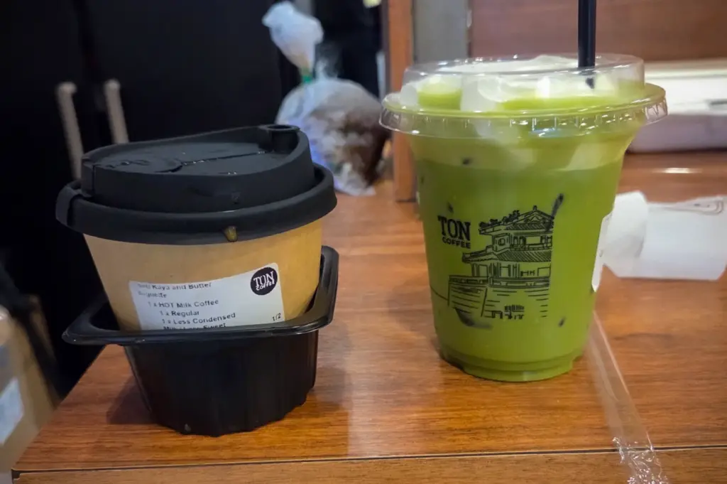 Hot coffee and iced matcha latte from TON Coffee Singapore, served in branded takeaway cups on a wooden counter, showcasing the café's specialty beverage selection.