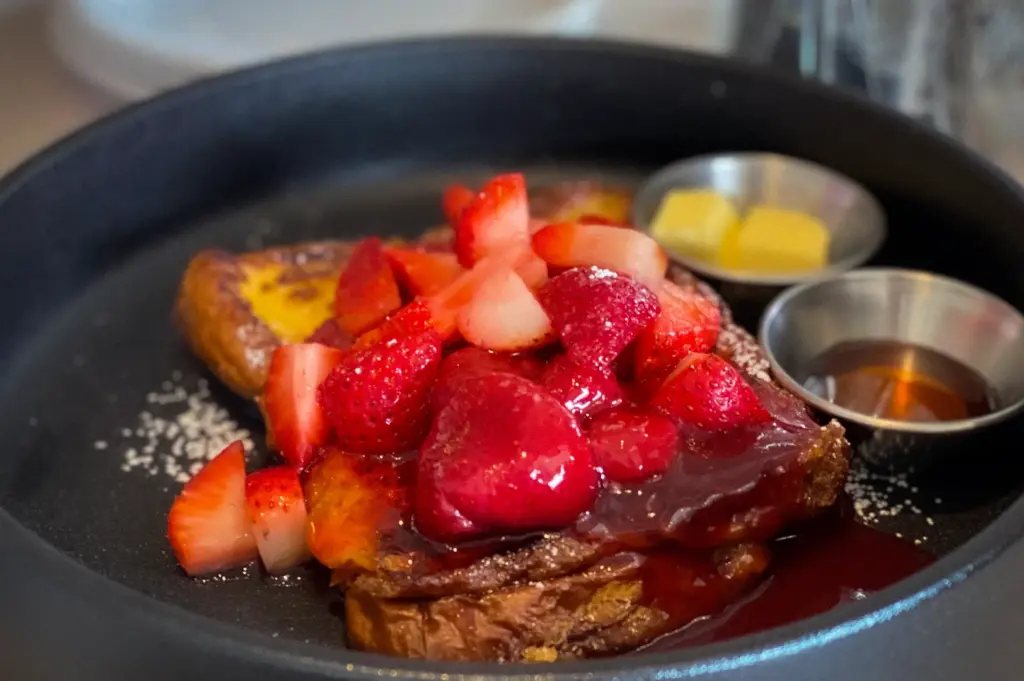 Brioche French toast topped with fresh strawberries and berry compote, served with butter and maple syrup at Atlas Coffeehouse in Bukit Timah, Singapore.