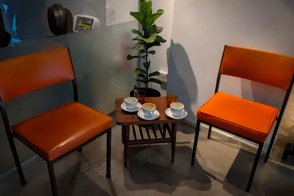 Coffee tasting setup at Nylon Coffee Roasters Singapore with espresso cups on a small wooden table between orange chairs in a minimalist café interior.