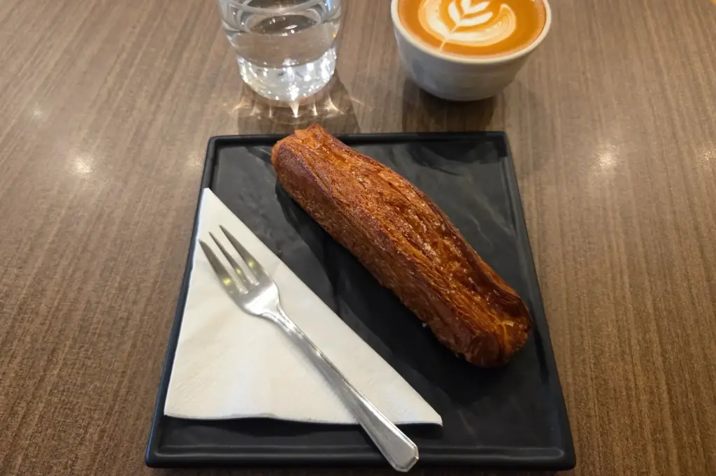 Freshly baked pastry served with a specialty latte featuring latte art and a glass of water at Tiong Hoe Specialty Coffee Roastery and Cafe Mastery in Singapore.