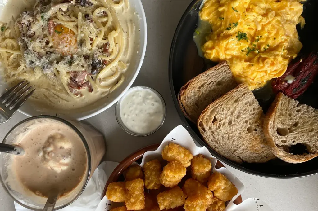 Atlas Coffeehouse brunch spread featuring creamy carbonara, scrambled eggs on sourdough, crispy tater tots with dip, and an iced coffee in Bukit Timah, Singapore.