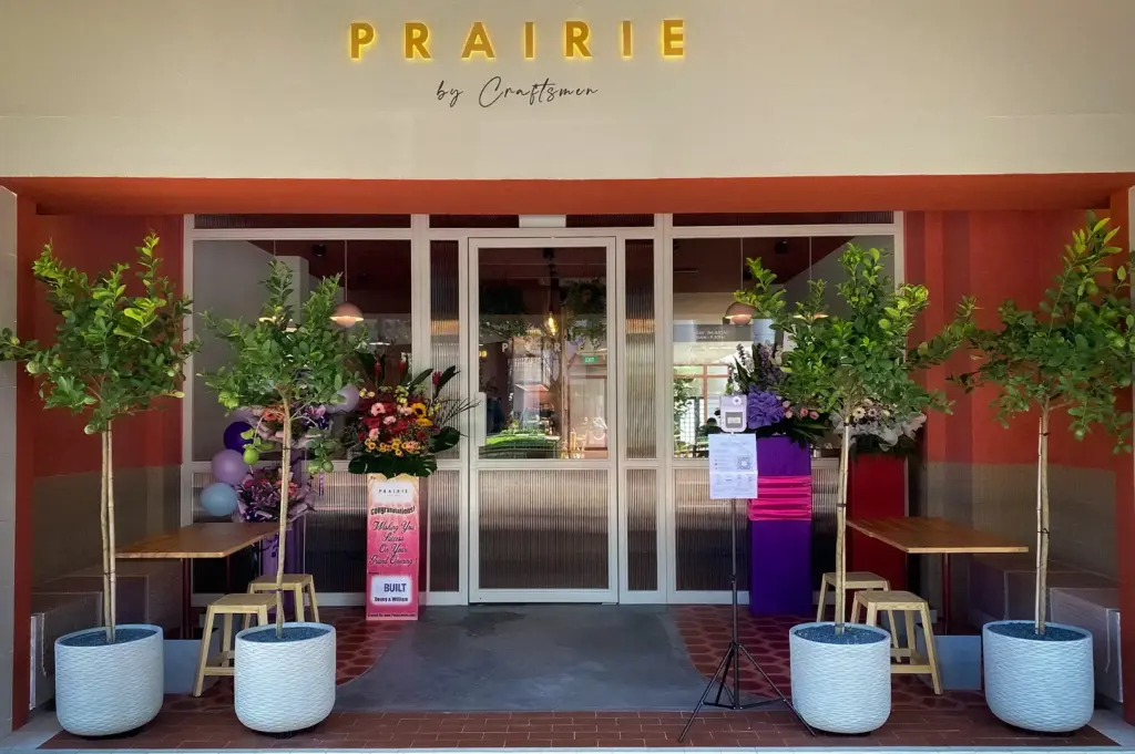 Front entrance of Prairie by Craftsmen in Singapore with modern café façade, potted trees, and inviting outdoor seating in a contemporary neighborhood setting.