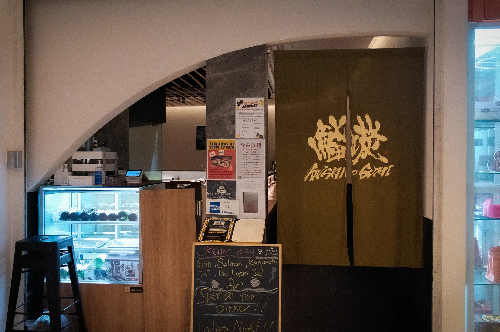 Sushi to Sumi Singapore restaurant entrance with Japanese noren curtains, sushi display case, menu board, and dining area