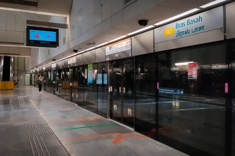 Bras Basah MRT Station platform in Singapore featuring platform screen doors, clear directional signage, and a clean modern underground transit environment.