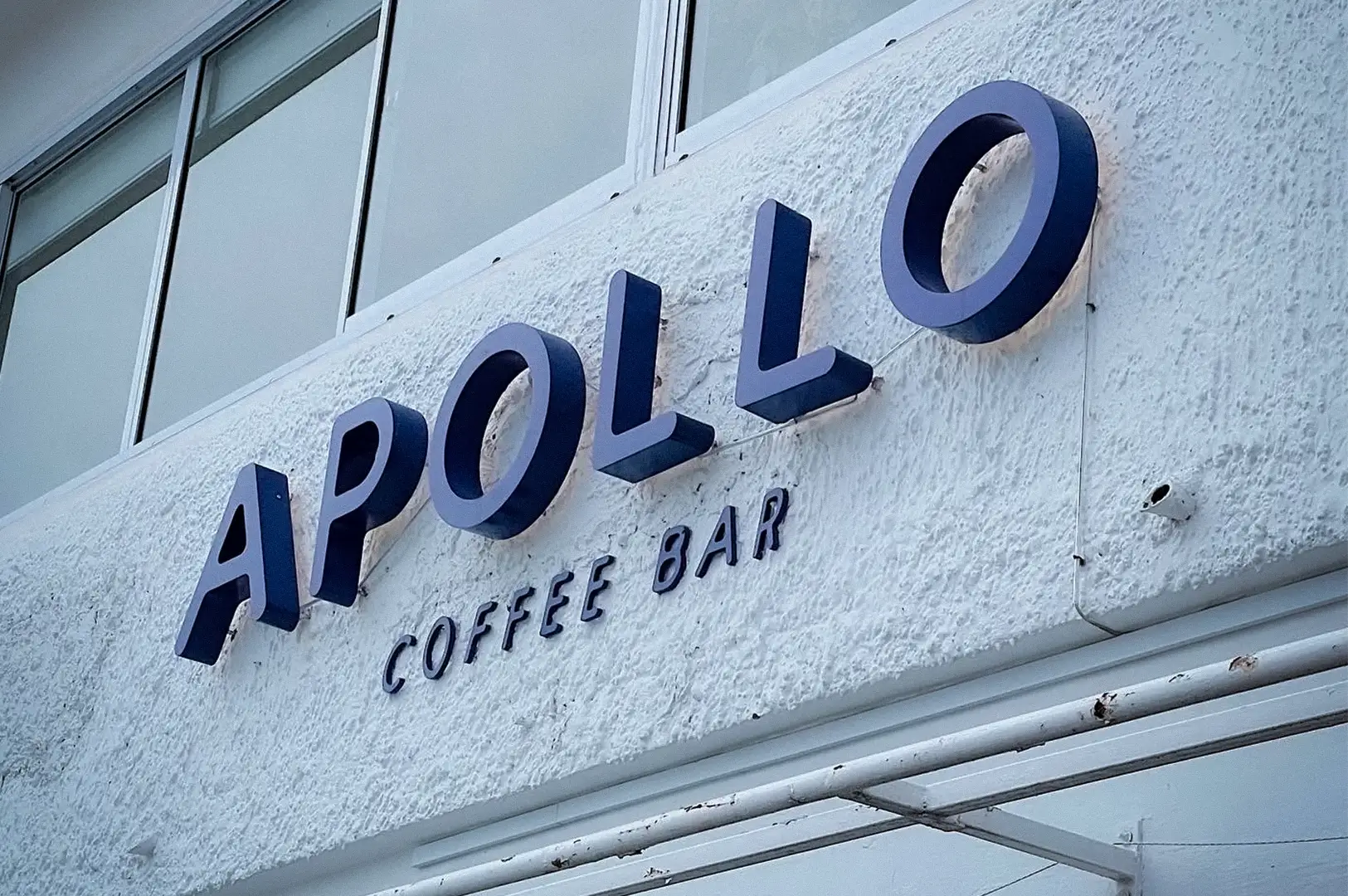 Exterior signage of Apollo Coffee Bar in Serangoon Gardens, Singapore, featuring the café's minimalist white facade and bold blue lettering above the entrance.
