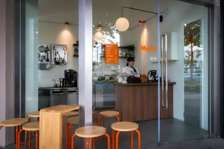 Moof Singapore cafe interior with orange stools, wooden tables, minimalist decor, coffee counter, and barista behind the register