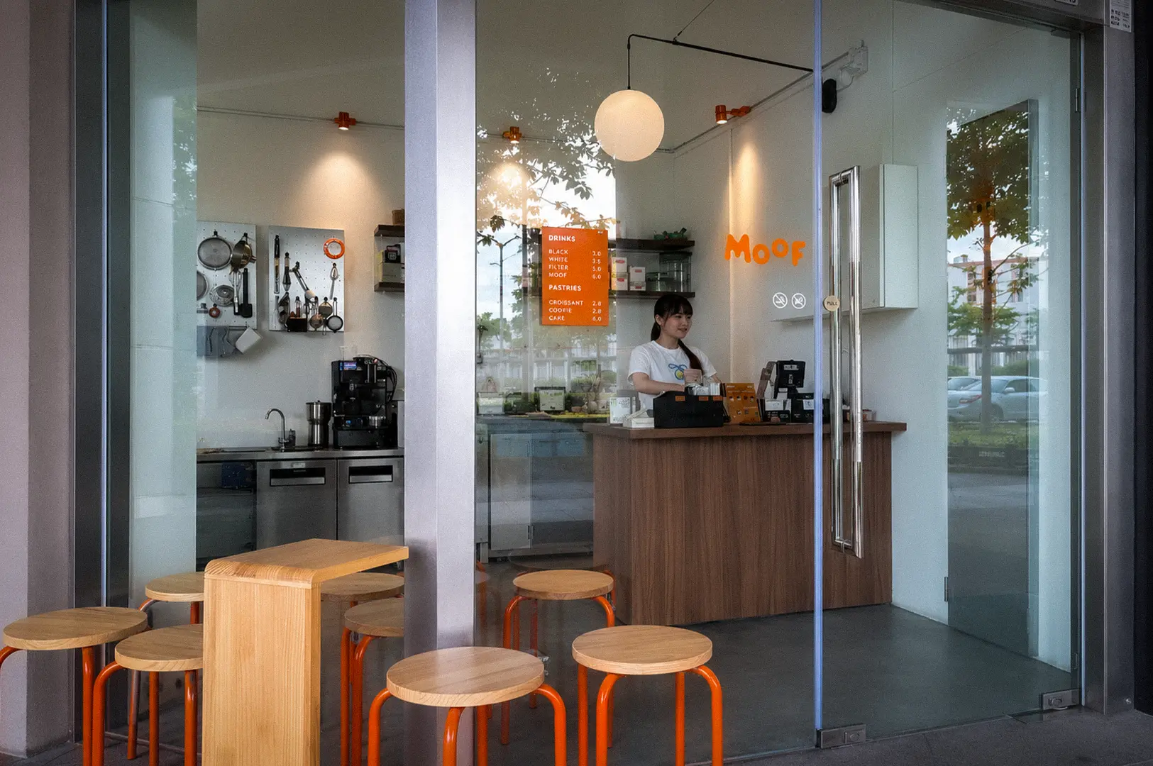 Moof Singapore cafe interior with orange stools, wooden tables, minimalist decor, coffee counter, and barista behind the register