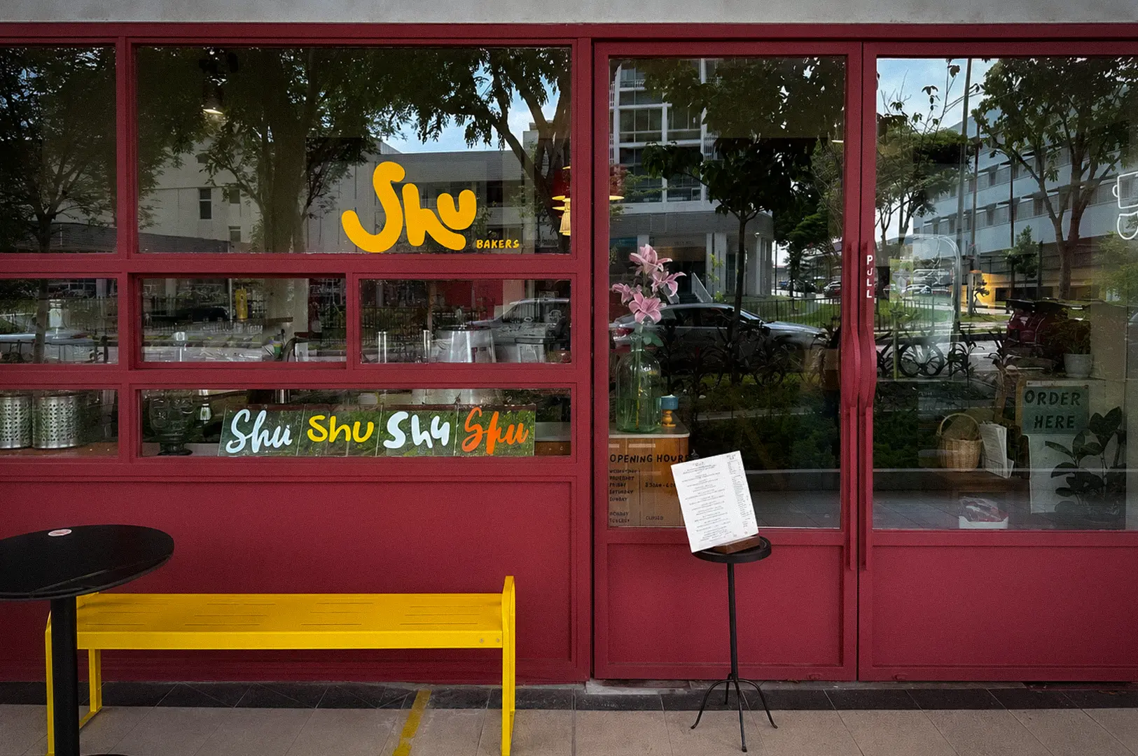 Shu Bakery Space@Kovan Singapore storefront with red-framed windows, yellow bench, and Shu Bakers logo.