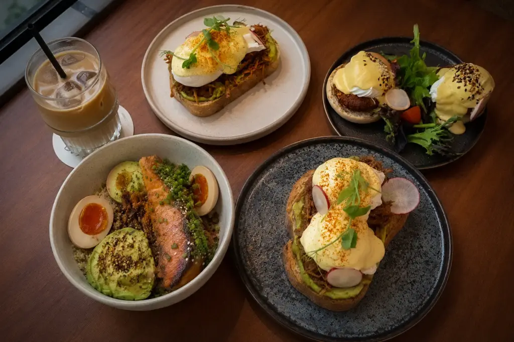 Lola’s Cafe Holland Village breakfast spread with salmon avocado bowl, poached egg toast, eggs Benedict, and iced coffee in Singapore