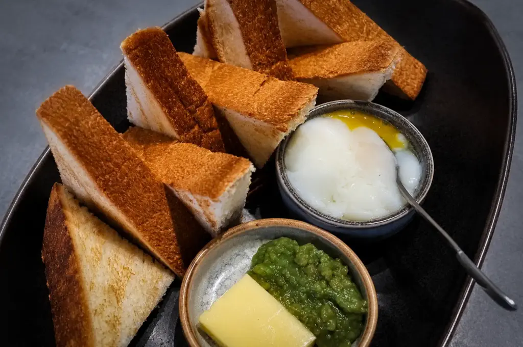 Homeground Coffee Roasters kaya toast with butter, kaya spread, and soft-boiled eggs served on a black plate