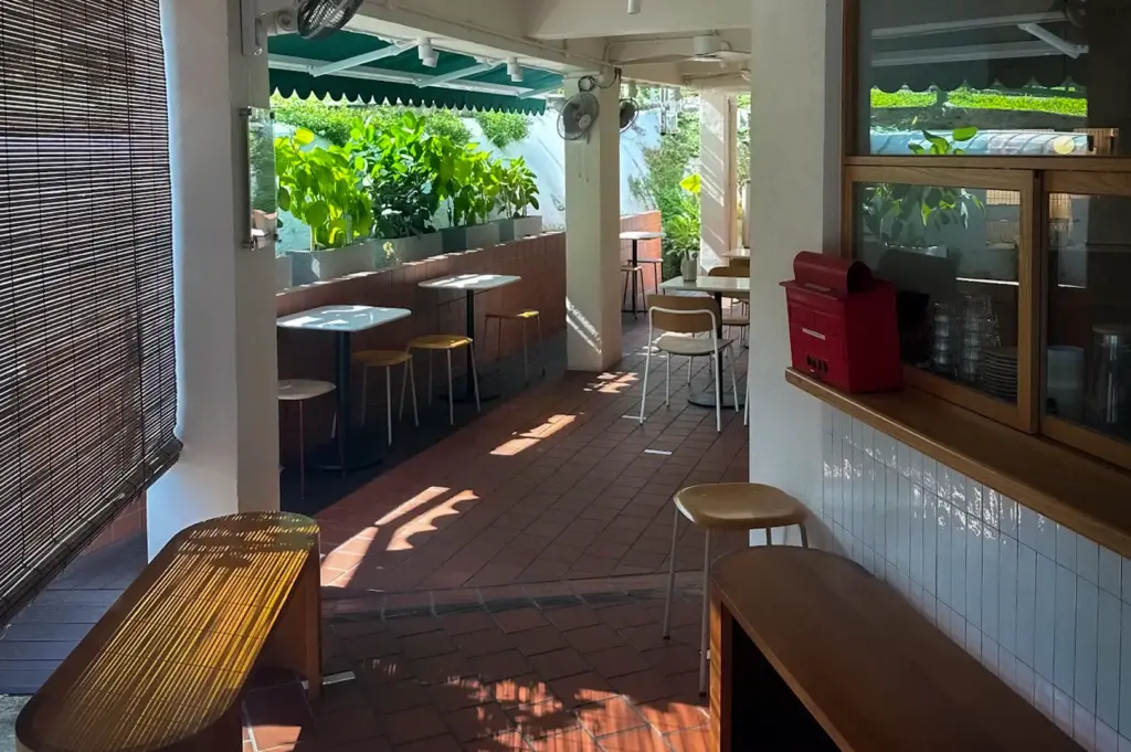 Lola’s Cafe Holland Village interior with outdoor seating, wooden furniture, tiled floors, green awnings, and lush plants in Singapore