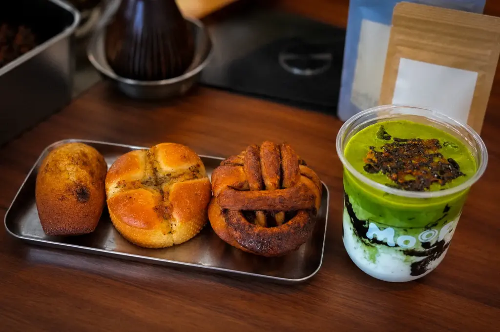 Moof Singapore pastries served with a matcha yogurt drink, featuring assorted baked breads and pastries on a metal tray