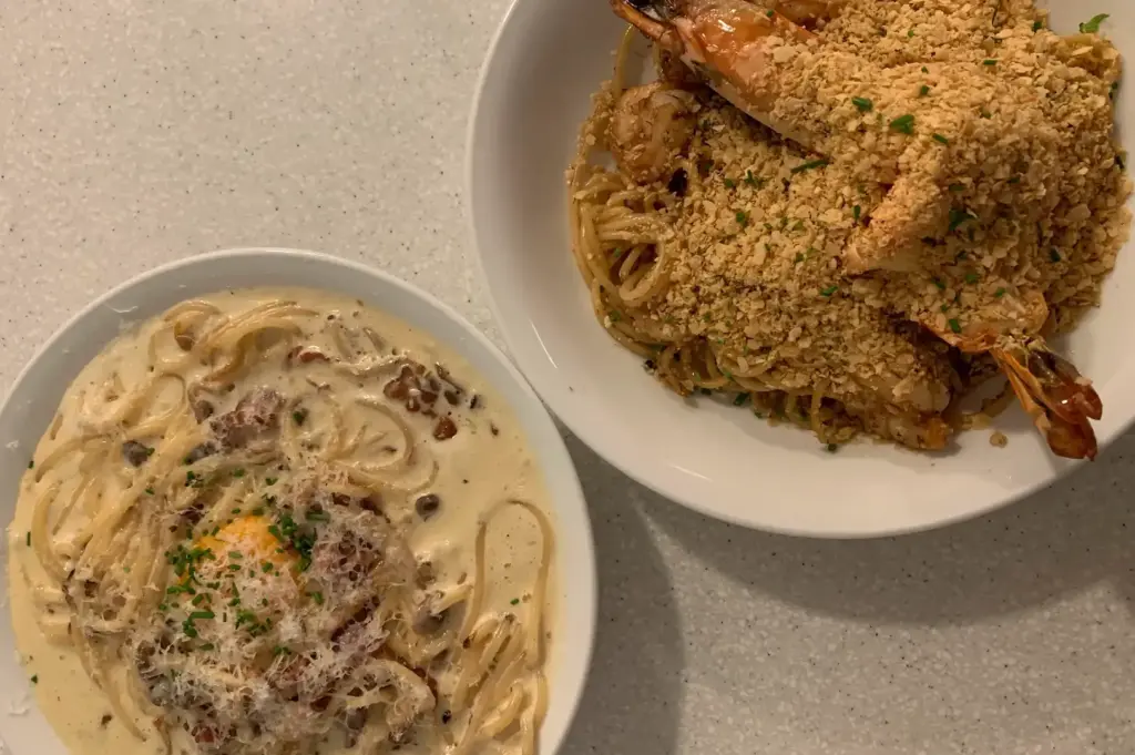 Creamy carbonara topped with a soft egg and parmesan alongside garlic prawn pasta at Apollo Coffee Bar in Serangoon Gardens, Singapore.