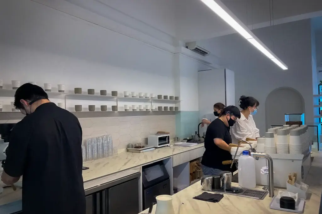 Equate Coffee Singapore baristas preparing coffee behind a minimalist white marble counter with ceramic cups and modern cafe equipment.