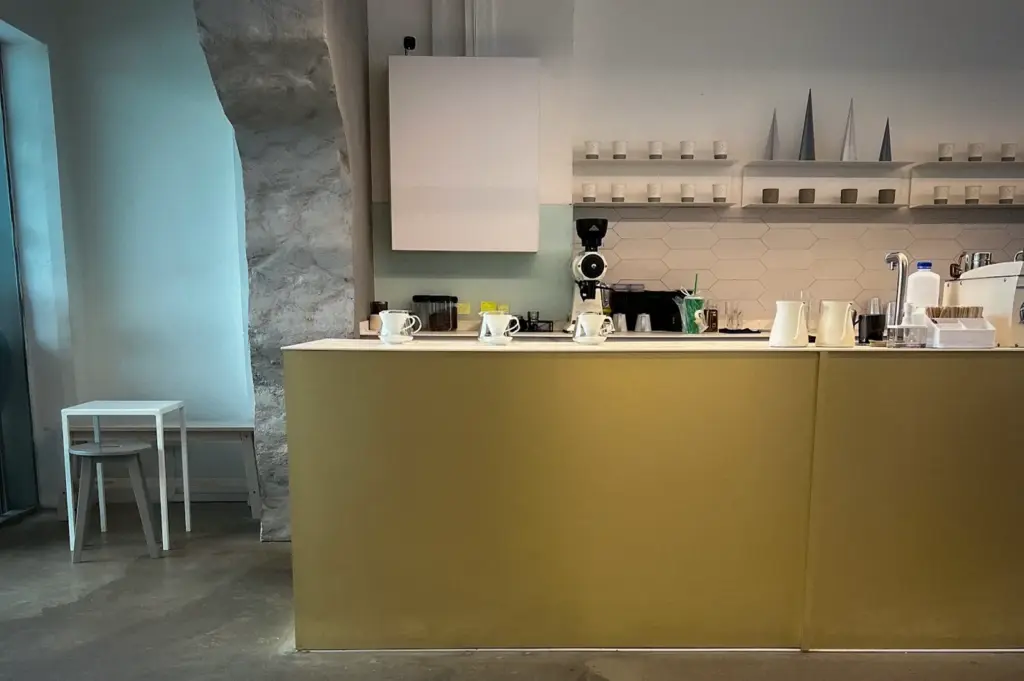 Equate Coffee Singapore minimalist cafe interior with a white coffee counter, ceramic cup display, exposed concrete walls, and modern coffee equipment.