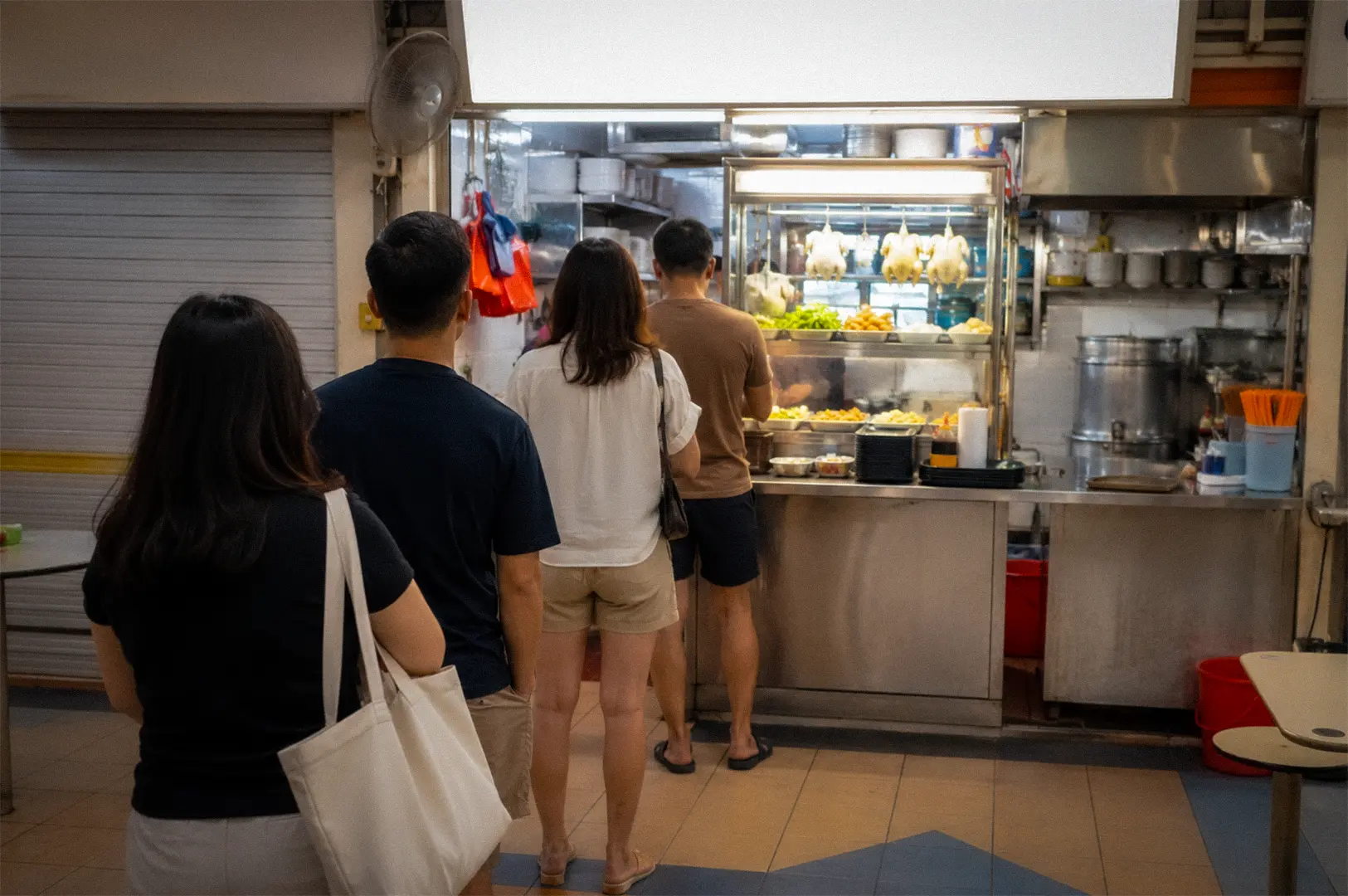 Customers queue at a Singapore hawker centre chicken rice stall with roasted chickens on display