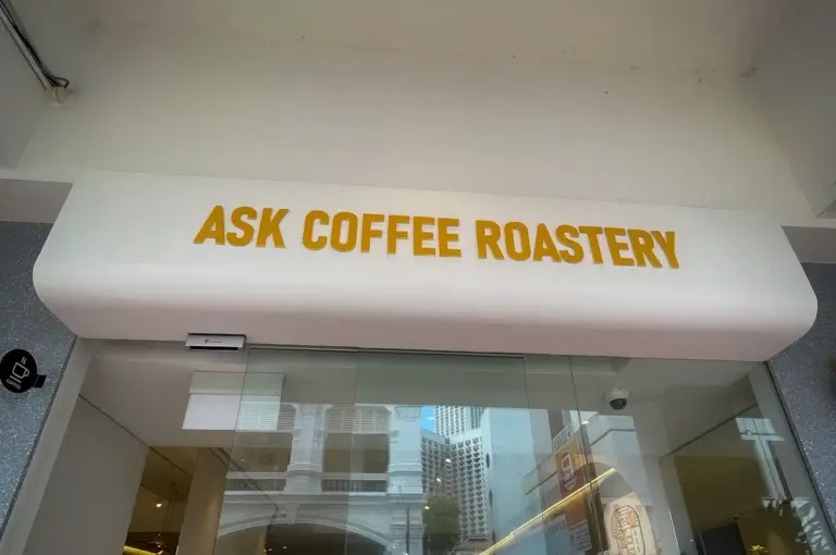 ASK Coffee Roastery Singapore storefront with glass entrance, cafe seating, and city street reflections