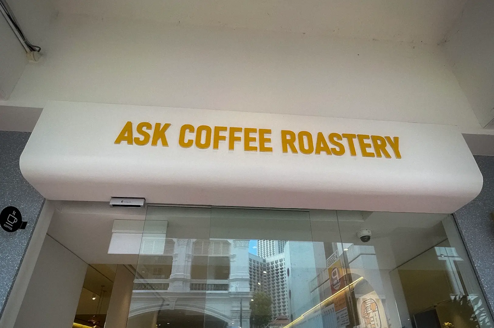 ASK Coffee Roastery Singapore storefront with glass entrance, cafe seating, and city street reflections
