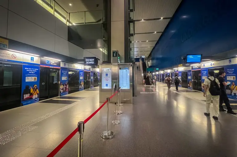 The modern platform interior of Expo MRT Station on the Downtown Line in Singapore, featuring blue-accented screen doors, clean tiled flooring, and waiting passengers.